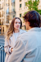 Young woman talking with a man, enjoying a casual conversation on a city street. Couple having an...