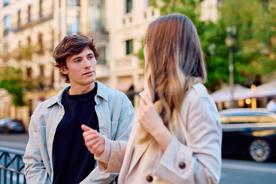 Young man listening intently, engaging in a conversation with a woman on an urban city street with buildings in background