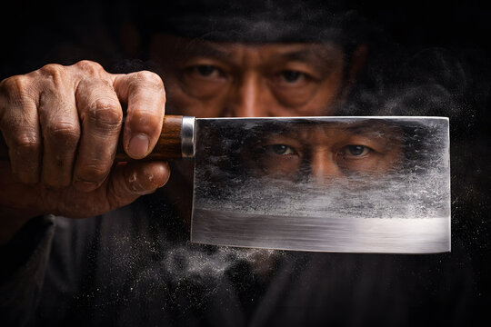 Intense close-up of a professional chef holding a large Cai Dao cleaver, his eyes reflected in the sharp steel blade. Dramatic cinematic lighting on a dark black background.