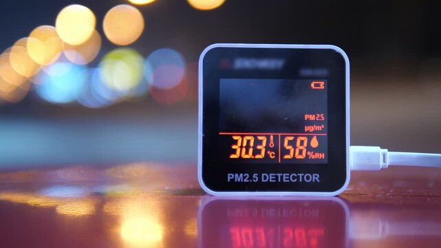 Digital PM 2.5 detector showing unhealthy air pollution levels with city traffic light bokeh background at night