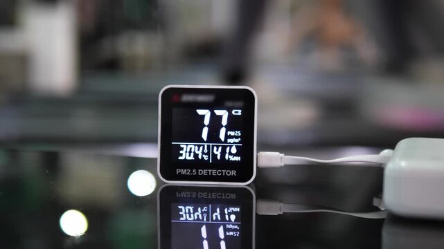 Close-up of modern digital PM 2.5 detector showing unhealthy air quality levels on reflective black surface