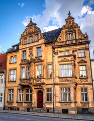 Fototapeta premium An ornate, multi-story building with symmetrical design, featuring detailed stonework, windows, and a red door, under a blue sky