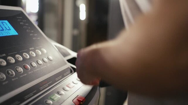 Close-up of a treadmill control panel during a home workout. Treadmill console with speed and incline buttons. A man's hand is visible near the controls. Concept of cardio training, fitness technology