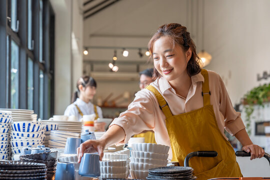 shop assistant restocking ceramic bowls from cart on the display shelf,asian employees working together to prepare merchandise for service customer in a modern pottery household shop