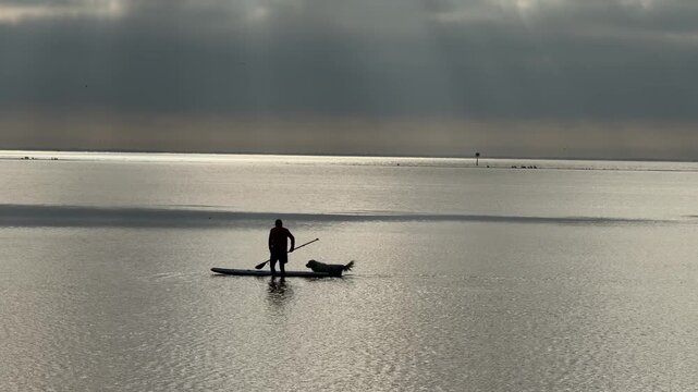Silhouette of a man and a dog riding a paddleboard