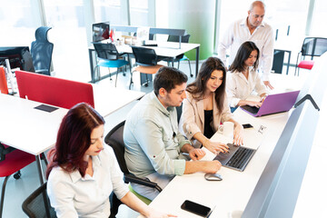 Fototapeta premium colleagues collaborate on projects using laptops at a long desk in a bright, office space with large windows. They work in a meeting or brainstorming.