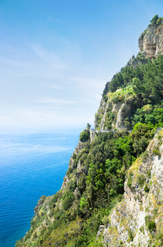 Coastal road along the cliffs of Amalfi Coast, Italy, with views of Mediterranean Sea. Rugged mountains and lush greenery in sunny day