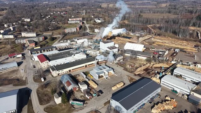 Aerial view of industrial complex with smoke rising from chimneys, wooden logs stacked, and buildings in a rural setting