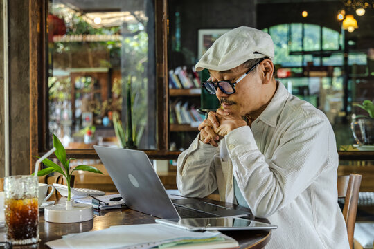 Senior entrepreneur typing on laptop managing small business operations, handling planning, documents, workflow, and digital tasks in cafe workspace focused on productive technology, elderly lifestyle