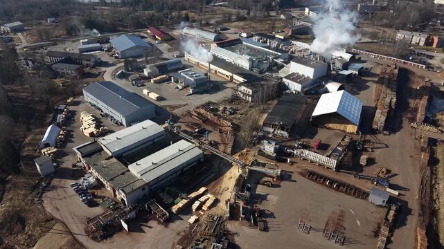 Aerial view of industrial lumber yard showing machinery, storage buildings, and smoke rising from processing areas in a busy landscape