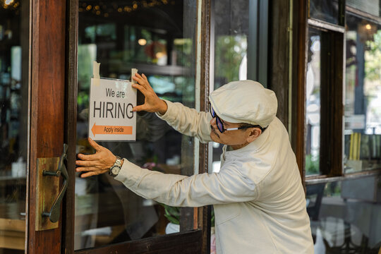 Senior small business owner reviewing work with his son, Asian 60s healthy senior barista entrepreneur holding hiring sign board pose at door, recruitment for new staff, expanding retail business