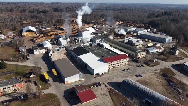 Aerial view of industrial lumber processing facility with smoke stacks, storage areas, and surrounding forest landscape in the background