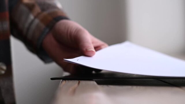 young caucasian woman in warm plaid shirt holding in hands blue stapler and stapling sheets of paper, selective focus, close-up view of hands