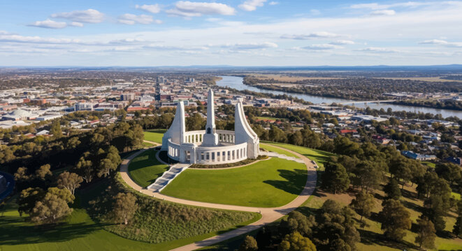 An aerial view showcases the majestic Australian War Memorial situated on Mount Ainslie, overlooking Canberra's vast cityscape and the scenic Molonglo River under a clear sky.