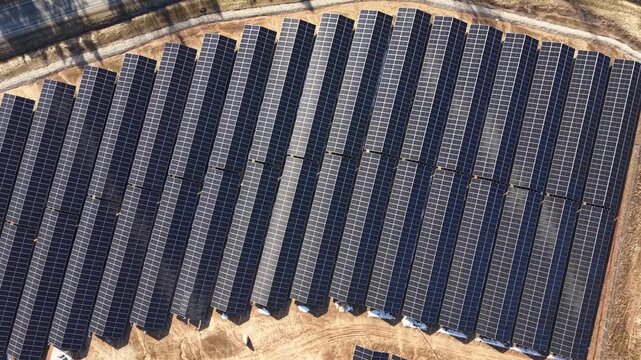 Aerial view of solar panel installation showing rows of photovoltaic modules arranged in a grid pattern on a sunny day in a renewable energy field