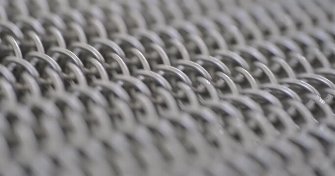 Conveyor is in operation, conveyor belt made of flexible stainless steel mesh is moving. Close-up handheld indoors shot, real time speed.