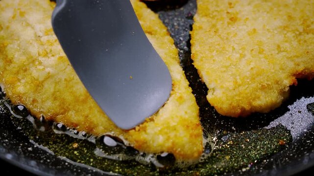 Frying breaded fish. Frying breaded fish. Frying flounder. Closeup breaded cutlet sizzling in pan, spatula pressing golden crust while oil bubbles and crumbs brown cozy kitchen scene showing