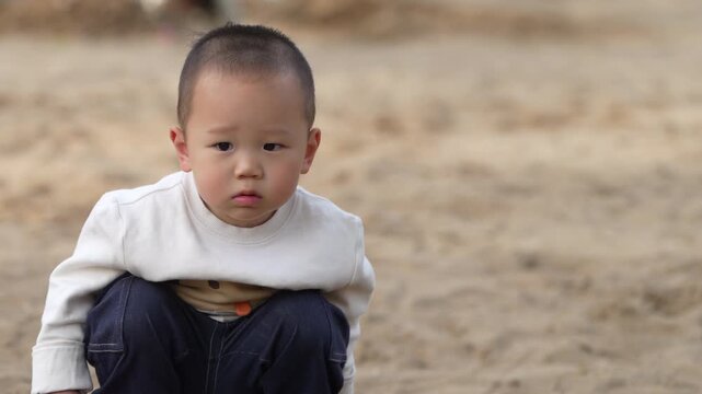 Portrait of a Little Asian Boy Squatting on the Sand Outdoors.