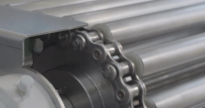 A stainless steel conveyor belt moves, driven by a chain transmission. Close-up handheld indoors shot, real time speed.