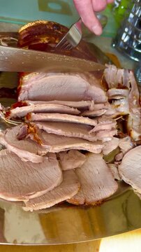 A joint of roast pork being carved into slices with a knife
