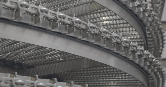 A multi-tiered spiral conveyor in operation, stainless steel mesh belts are moving. A working transport system with an axisless spiral. Close-up handheld indoors shot, real time speed.