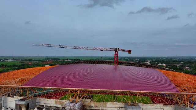 Aerial video: red crane on a large domed stadium roof under construction.
