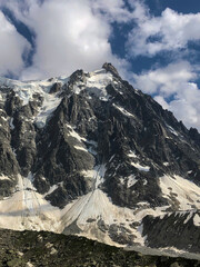 Aiguille du Midi, Mont blanc massif showing rugged rock faces and expansive glaciers under a dynamic sky with white clouds, highlighting the grandeur of the alps - stock photo