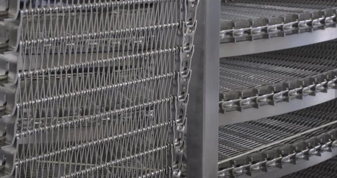 A multi-tiered spiral conveyor in operation, stainless steel mesh belts moving in different directions. A working transport system with an axisless spiral. Close-up handheld indoors shot, real time sp