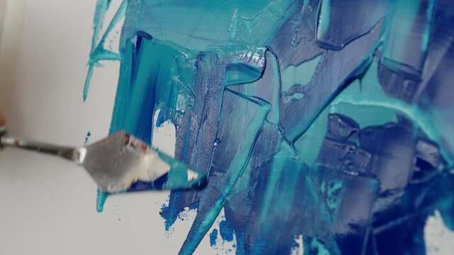 Macro view of a palette knife spreading thick teal and blue paint across a white canvas, creating glossy impasto textures, layered strokes, and drips in an abstract art process