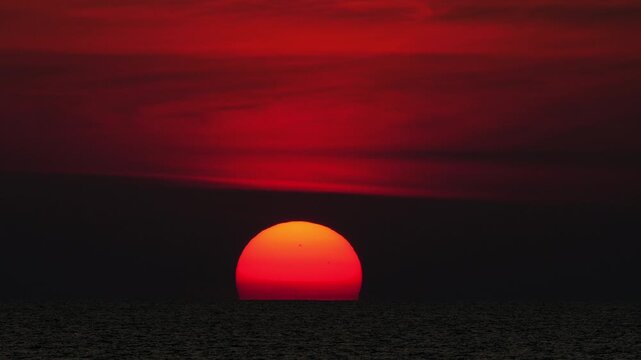 Golden sunset over the sea, captured from a scenic viewpoint. The sun slowly dips below the horizon, casting warm orange and yellow tones. Peaceful and serene atmosphere