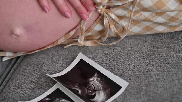 Pregnant woman looking at ultrasound images of her baby, emotional maternity moment and prenatal health check