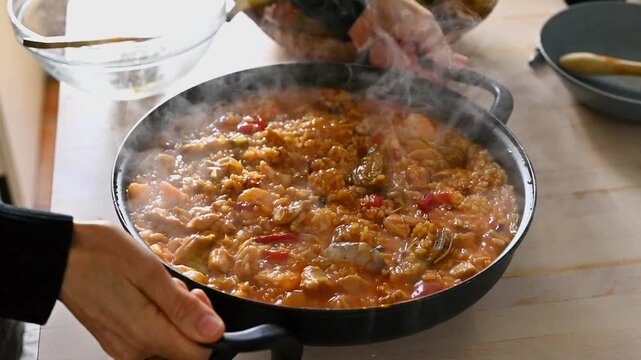 Close-up of female hands rotating electric paella pan to evenly cook rice traditional Spanish cooking technique at home, Rice recipes, soupy rice with chicken
