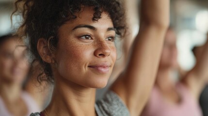 Obraz premium Close-up portrait of a young woman with curly hair. she is in a yoga class, with other people in the background. the woman is looking off to the side with a peaceful expression on her face.