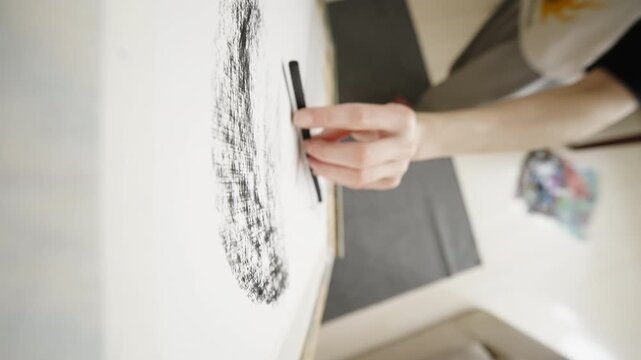Close-up of an artist s hand guiding a charcoal stick on white canvas, layering textured shading and expressive strokes in a bright studio, from first touch to final marks.