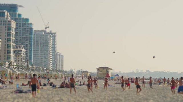 People enjoy playing at the beach in Tel Aviv Israel on hot sunny summer day. Locals and tourists swimming in sea and sunbathing on sand while others play with ball during vacation or weekend