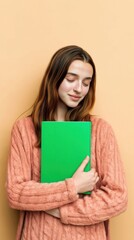Fototapeta premium Young Woman in Pink Cable Knit Sweater Holding Green Book Mockup standing against Beige Wall for Bookstore Promotion and Educational Advertising Background
