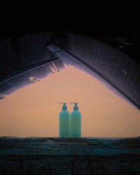 Two sage green cosmetic pump bottles standing on a stone ledge in a dark tropical setting for beauty brand packaging mockup and organic skincare advertising