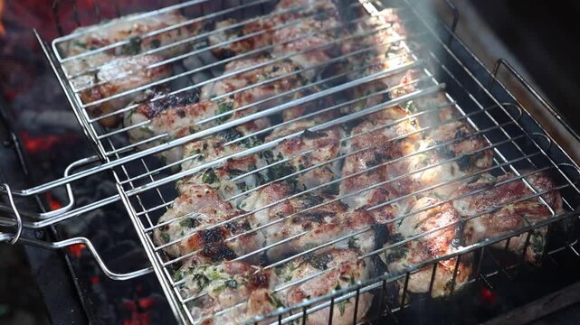 Appetizing shashlik, pork, meat is being grilled on a barbecue grate, on a mangal. A man is turning the meat
