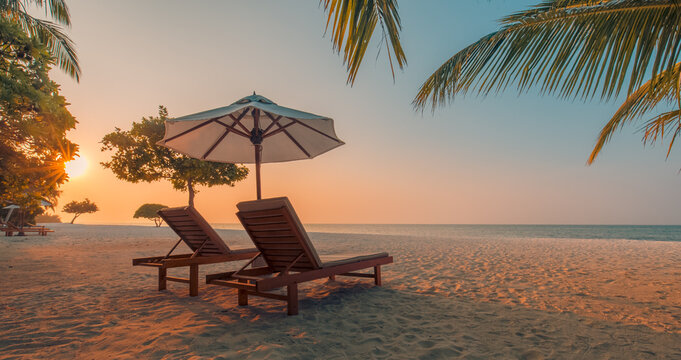 Gorgeous romantic sunset beach with elegant white sunbeds and palm leaf umbrella, breathtaking calm tropical ocean view, radiant golden sky and captivating luxury honeymoon summer vacation background