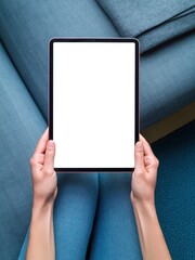 Naklejka premium Hands Holding Digital Tablet Mockup with Blank Screen over Blue Sofa in Cozy Living Room, Top View Flat Lay for Lifestyle App and Interior Design Marketing