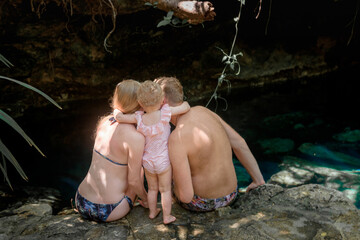Fototapeta premium Family sitting by cenote water with toddler
