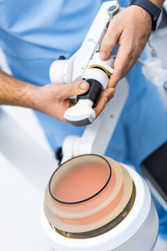 Medical professional adjusting extracorporeal shockwave lithotripsy device close up. Hands in blue scrubs holding medical equipment over ultrasound gel pad in clinic.