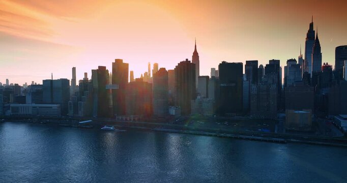 Skyscraper skyline of New York dazzled by the setting sun. Drone footage over the riverscape approaching densely built waterfront.