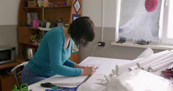 Dressmaking process. Tailor desk. Woman hand creating garment patterns with ruler making notes on paper in clothes studio interior.