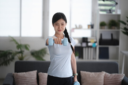 Asian woman uses a dumbbell at home to enhance her fitness and strength