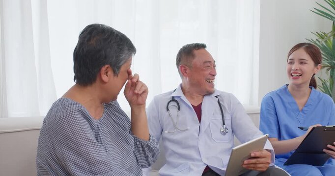 Senior Asian doctor laughing while holding a digital tablet in a bright clinic room, focusing on empathetic elderly care, positive patient experiences, and friendly healthcare communication.