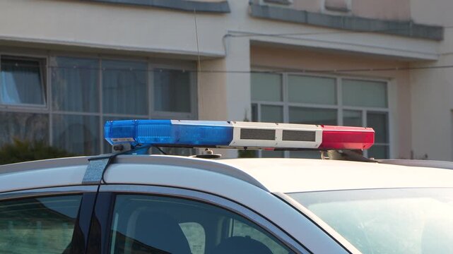 Close up side view showing silver patrol vehicle roof equipped with flashing blue and red led emergency strobe light bar parked on city street near building during daytime.