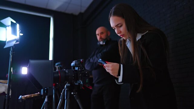 Long-haired Caucasian woman stands at the camera using her phone. Male photographer standing behind approaches a display.