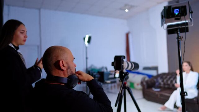 Focused cameraman sits at the camera looking at display. Crew works at the footage in studio for blog creation.