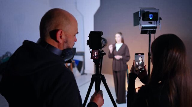 Male and female photographers are recording a woman in the blurred backdrop. Studio backstage work.